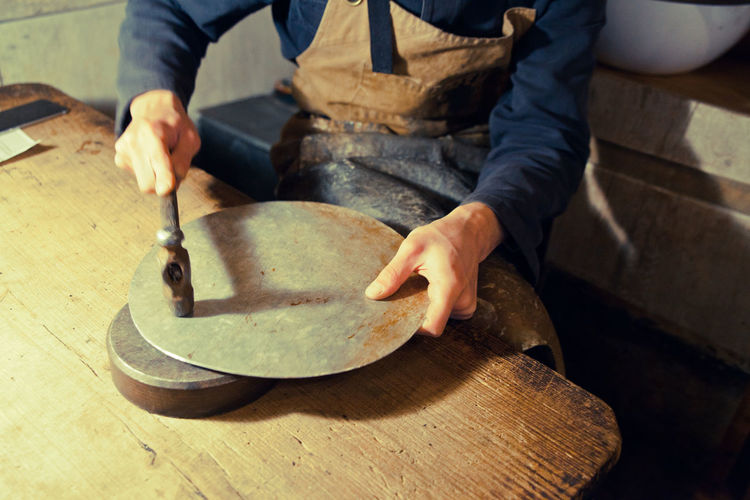 Midsection of worker hammering metallic plate in workshop