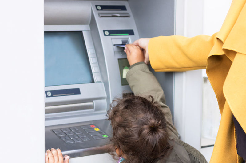 Midsection of mother teaching daughter to use atm machine