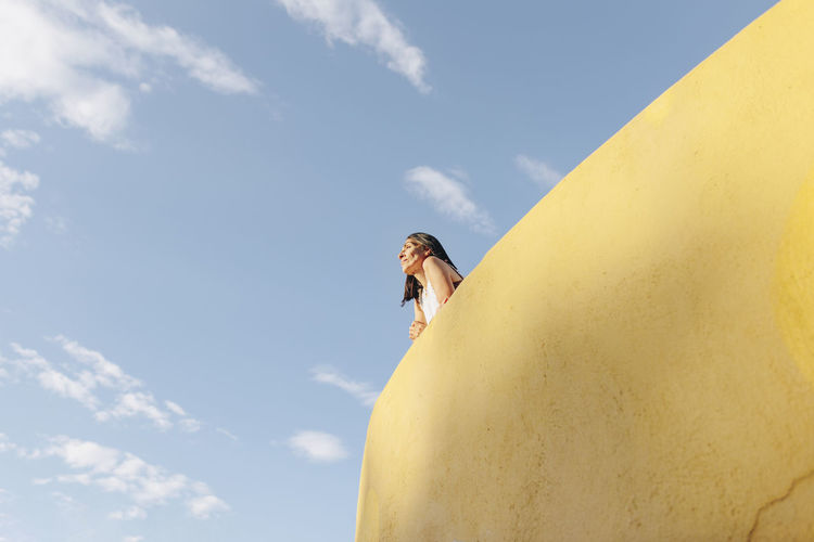 Low angle view of woman standing on cliff against sky