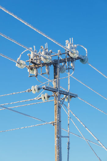 Low angle view of frozen electricity pylon against blue sky