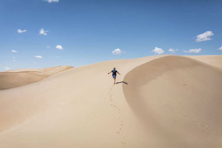 High angle view of carefree woman with arms outstretched walking on sand at great sand dunes national park during sunny day
