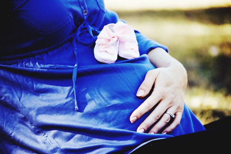 Midsection of pregnant woman with baby booties sitting outdoors