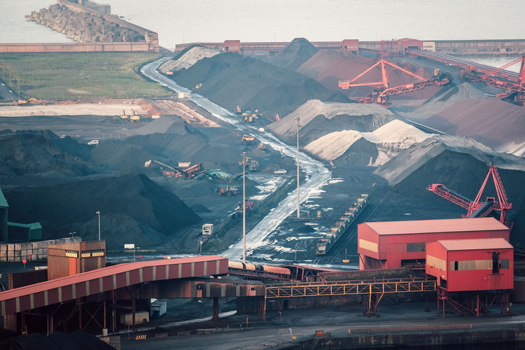 Aerial view of industrial coal extraction with working machines and piles of material at hazy shore