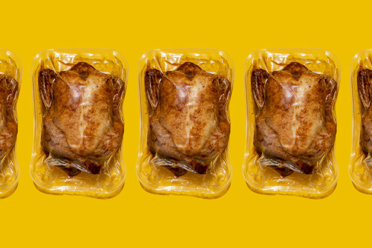 Vacuum packed roasted chickens arranged in a line on yellow background