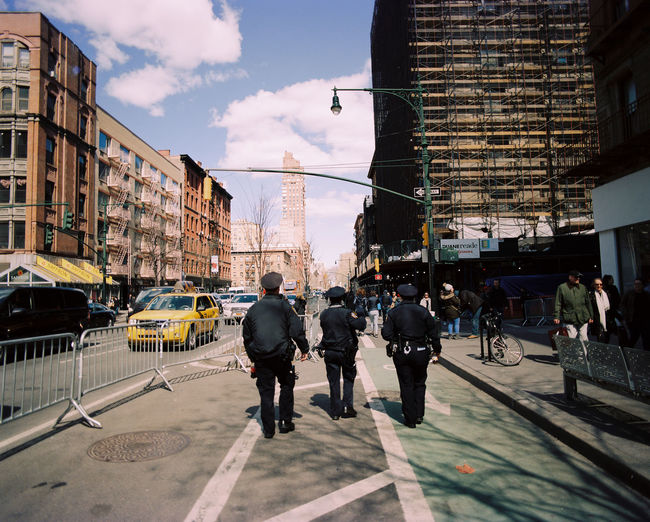 Rear view of police officers walking on sidewalk in city