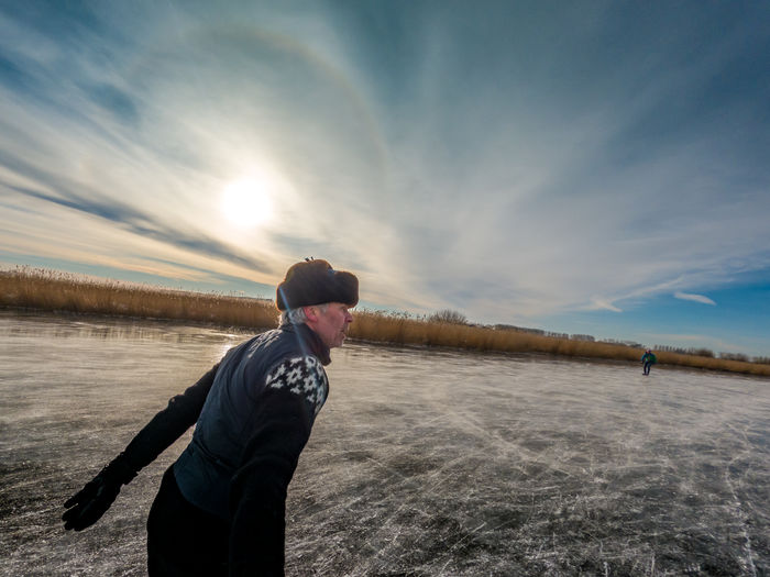Man skating on frozen lake against sky