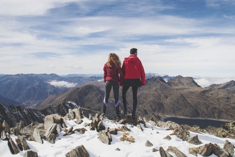 Rear view of men standing on snowcapped mountains against sky