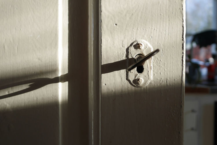 Close-up of a white painted vintage door closed with the key in the keyhole in shadow and light