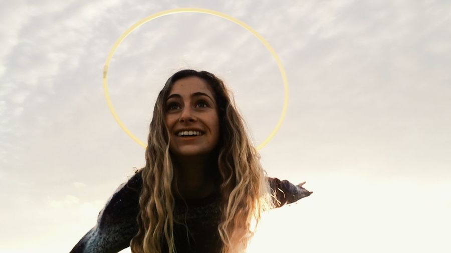 Low angle view of smiling young woman with plastic hoop against sky