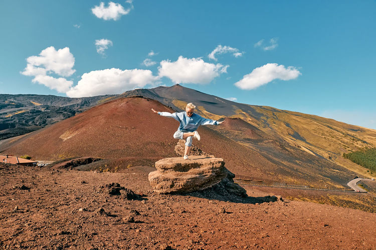 woman doing yoga on big stone at panoramic view of summits of active volcano etna