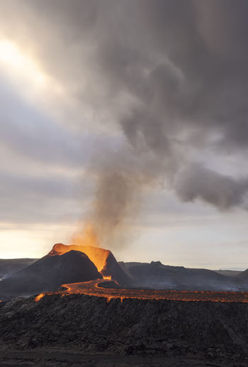 Splashes of hot orange lava erupting from volcanic mountain peak surrounded with smoke in iceland