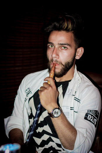 Portrait of young man smoking hookah in darkroom
