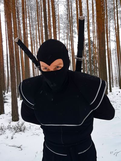 Man wearing black uniform with swords in forest during winter