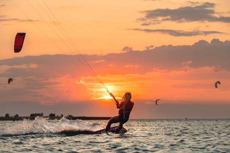 Young woman professional kiter performs ride beautiful background of the sunset and sea