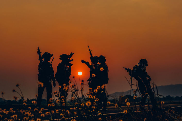 Silhouette soldiers against orange sky during sunset