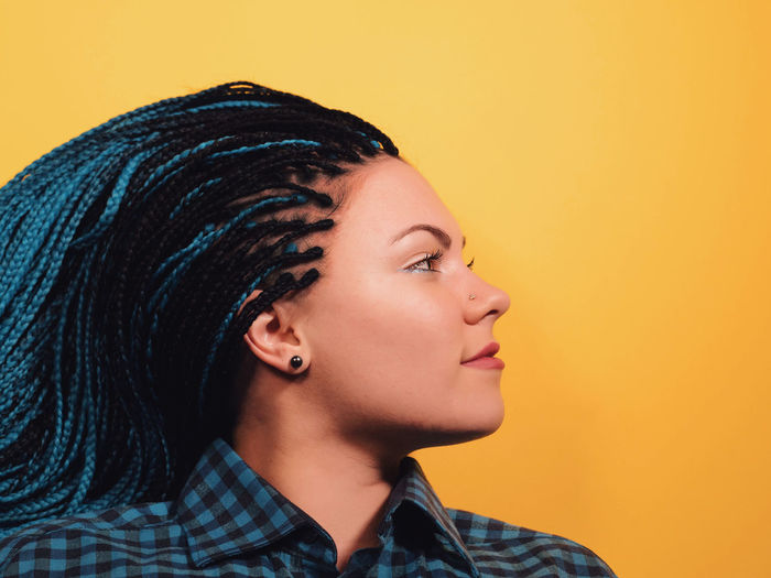 Close-up of young woman with braided hair against yellow background
