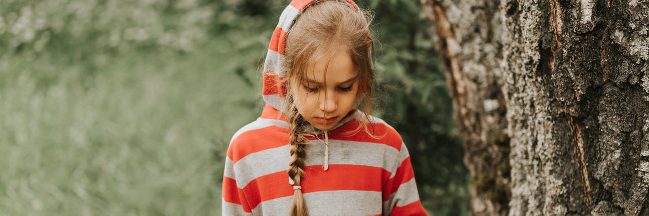Portrait face of upset or focused thoughtful scowl eight year old kid girl in hood of striped hoodie