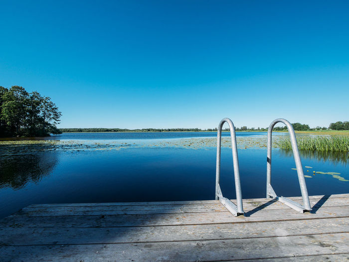 Swimming pool by lake against clear blue sky
