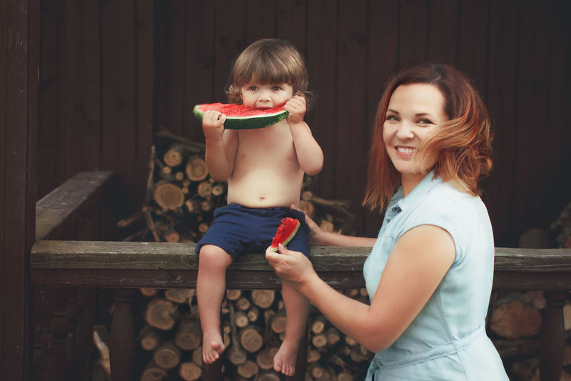 Portrait of smiling mother eating watermelon with son at home