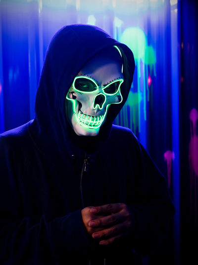 Serial killer wearing neon skull mask at halloween costume party with colorful background.