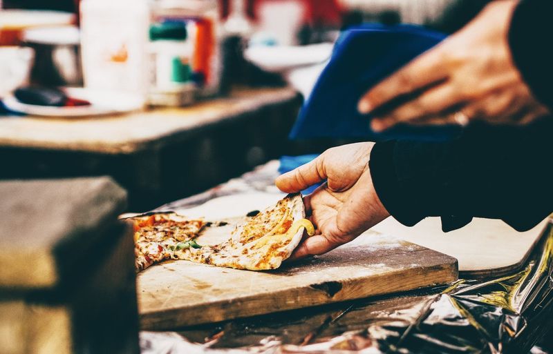 Cropped image of man holding pizza served on table