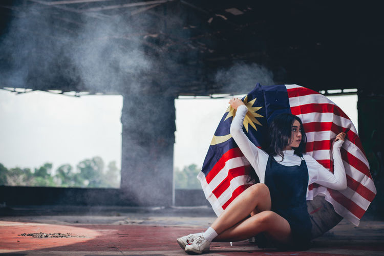 Young woman holding malaysian flag while sitting on floor