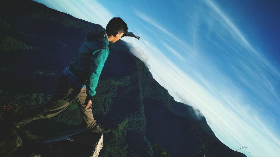 Tilt shot of man on mountain against blue sky