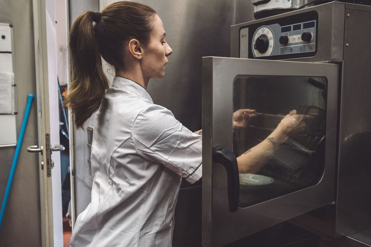 Side view of female chef putting dish in oven at commercial kitchen