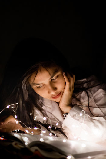 Close-up of woman with illuminated light reading book on bed at home
