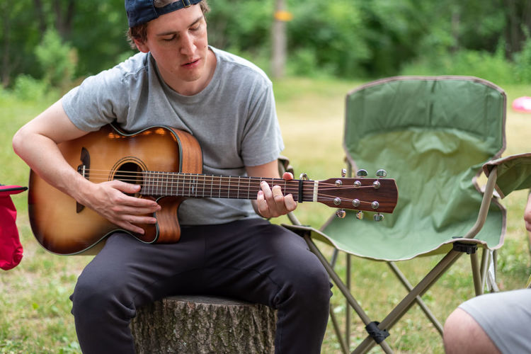 Casual young man playing guitar at a campsite in summer