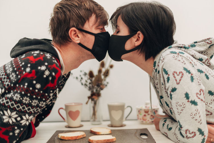 Side view of young man and woman wearing mask kissing at cafe