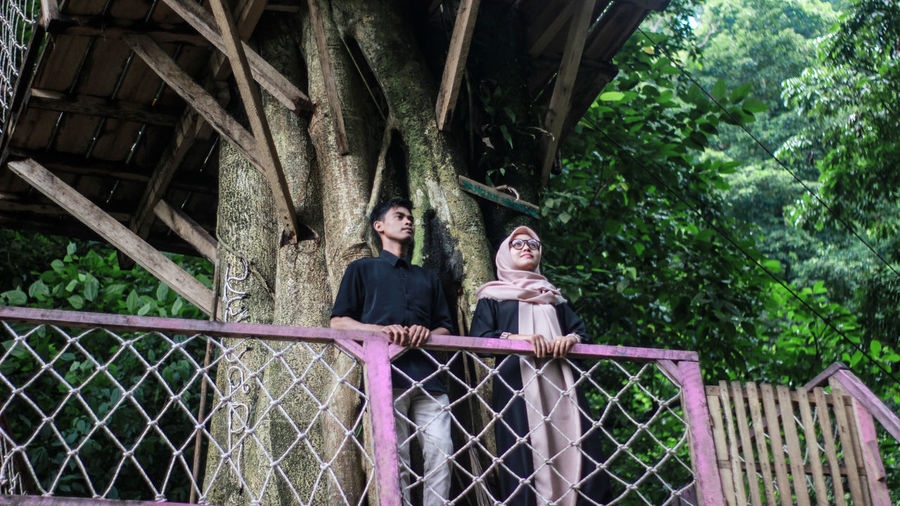 Man and woman on footbridge against trees in forest