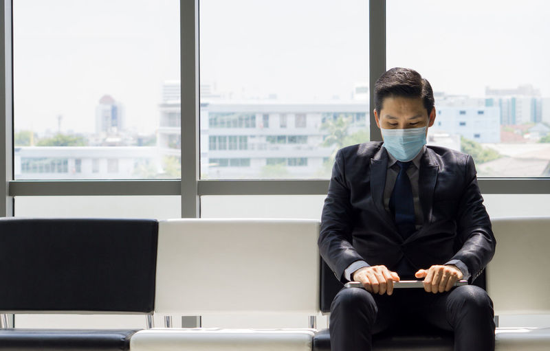 Man with mask sitting in waiting room in office