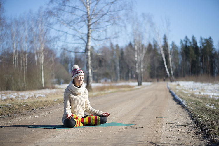 Woman yoga sitting and meditating in a lotus positionon on the rural road during  early spring