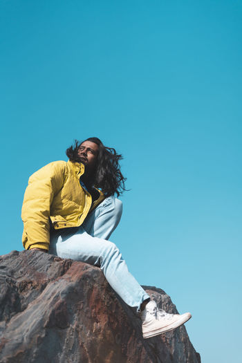 Young woman sitting against blue sky
