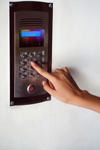 Cropped hand of woman using intercom on wall