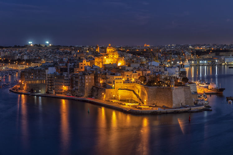 Illuminated buildings in city by sea at night