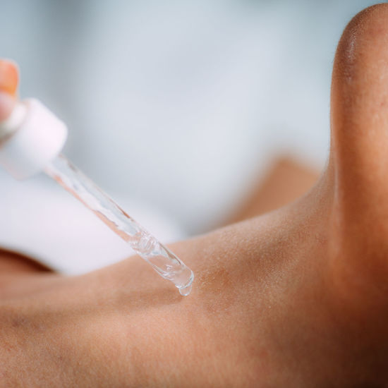 Neck anti-aging treatment. cosmetician applying hyaluronic acid serum on womans neck