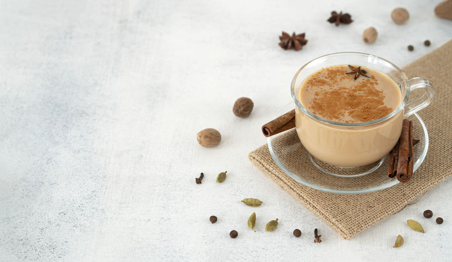 Traditional indian masala tea in a glass cup with cinnamon, ginger, cardamom, anise, honey, milk.