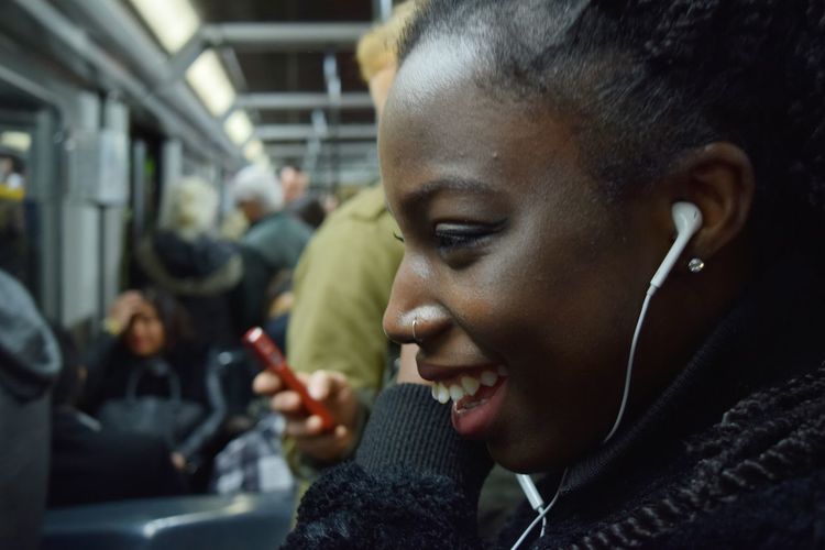Profile view of smiling young woman listening to music through in-ear headphones in train