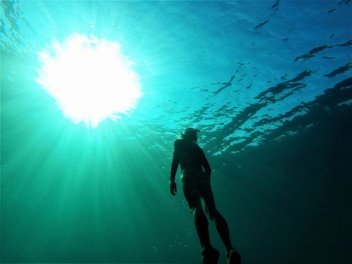 Low angle view of silhouette young man swimming in sea