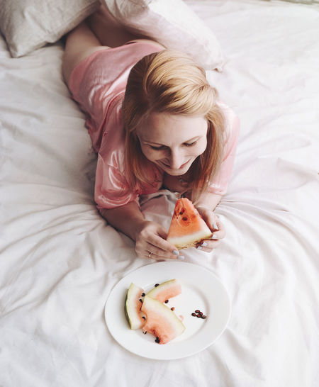High angle view of woman having watermelon on bed at home