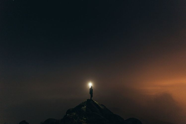 Silhouette person holding light on top of mountain against sky at night