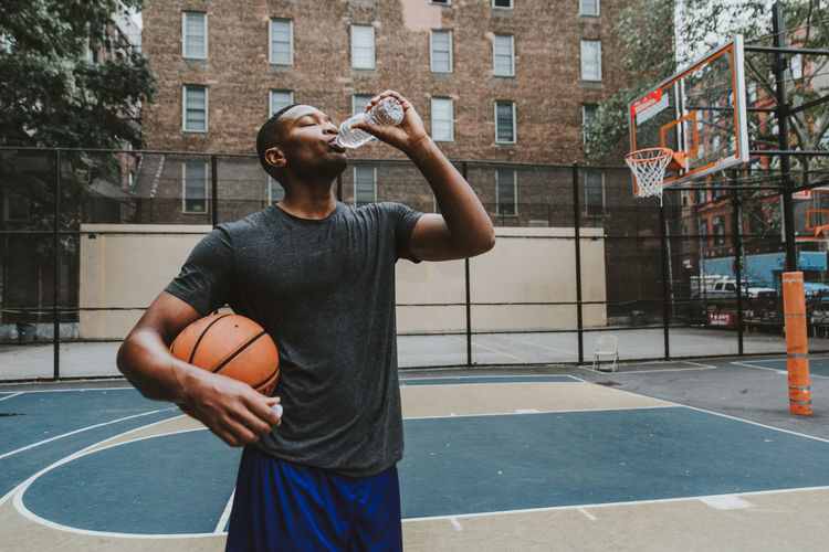 Male athlete holding basketball while drinking water in court