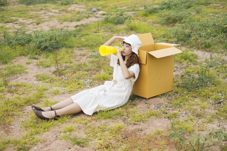Full length of woman sitting by cardboard box on grass
