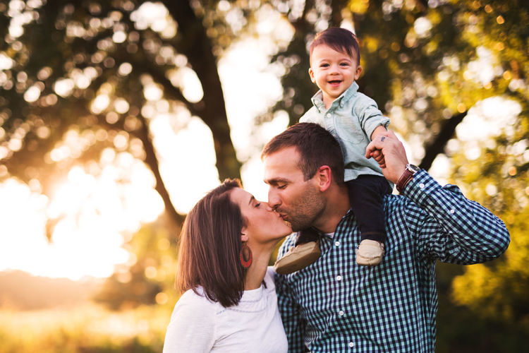 Portrait of cute smiling baby boy while parents kissing in park