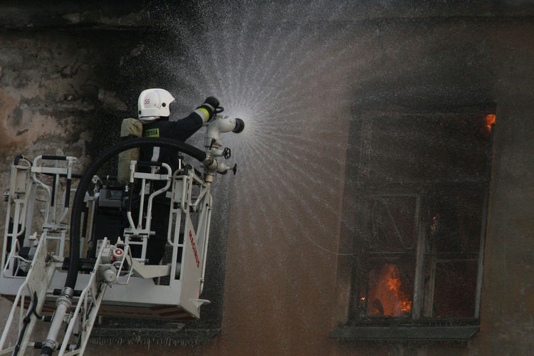 Rear view of firefighter on crane extinguishing fire in building