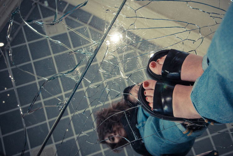Low section of woman standing on cracked glass floor with reflection