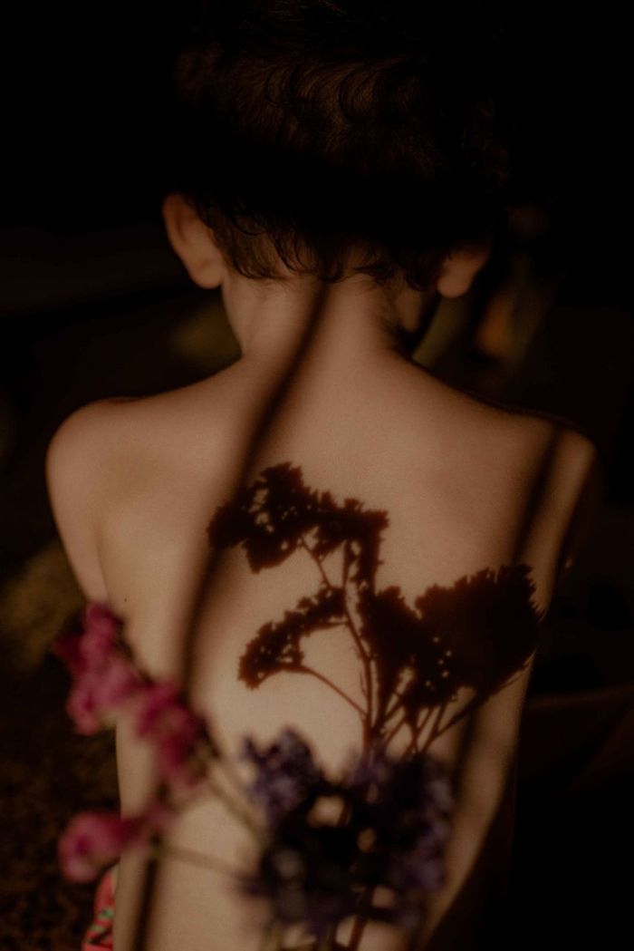 Shadow of flowers on shirtless boy back in darkroom