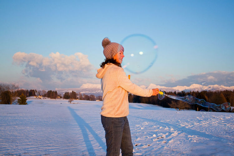 Rear view of woman blowing bubbles on snow covered land